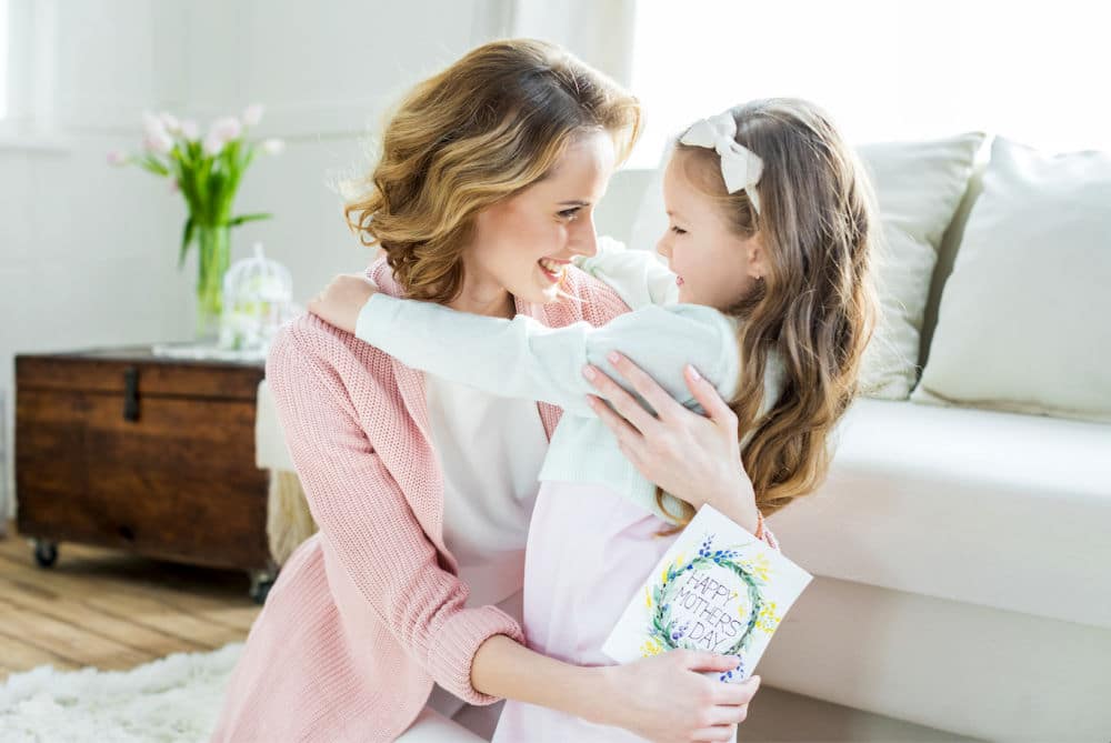 Mother and daughter with mothers day card hugging