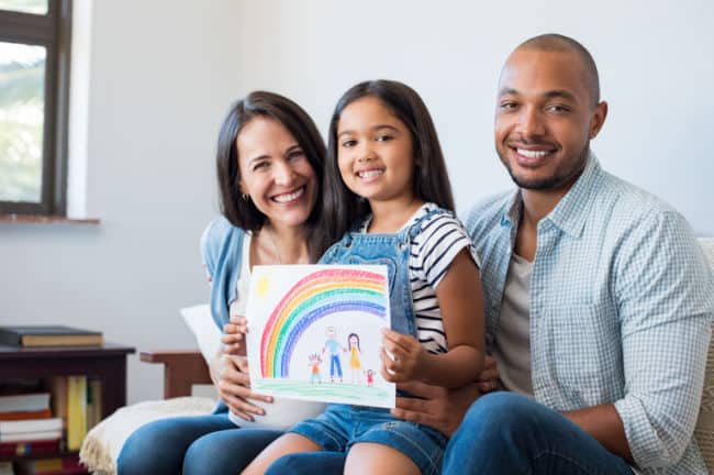 Child holding rainbow drawing with parents