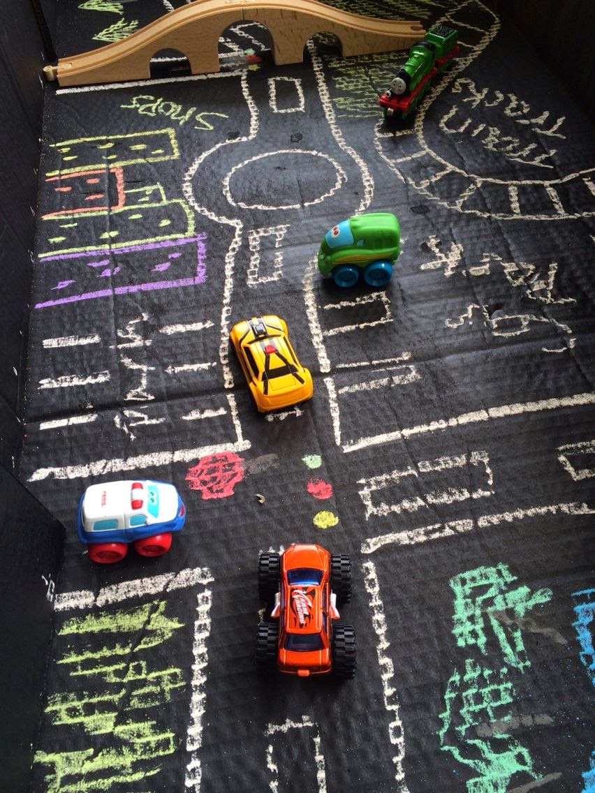 Chalk drawn town with roads in cardboard box and toy cars. 