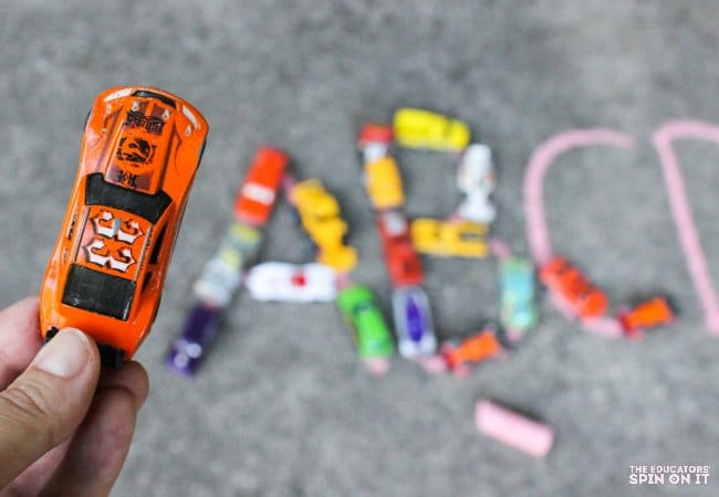 Child holding an orange toy car ready to build the letters in the alphabet.