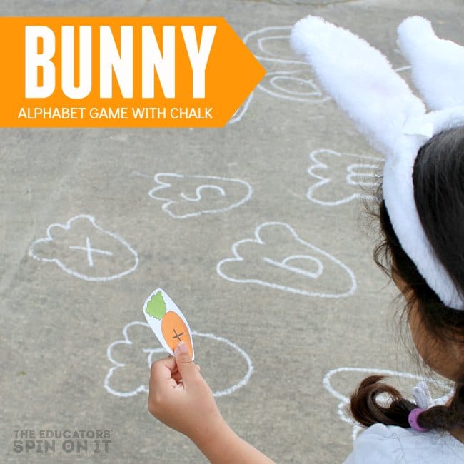 child holding paper carrot with letter looking for rabbit foot print with sidewalk chalk outdoors. 