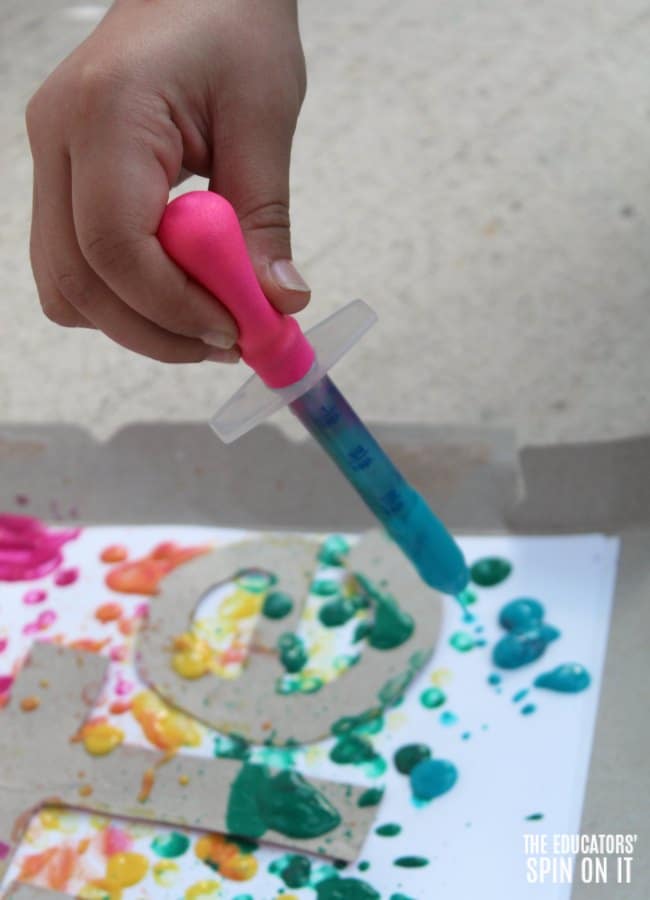 Child using medicine dropper to drip paint using rainbow colors