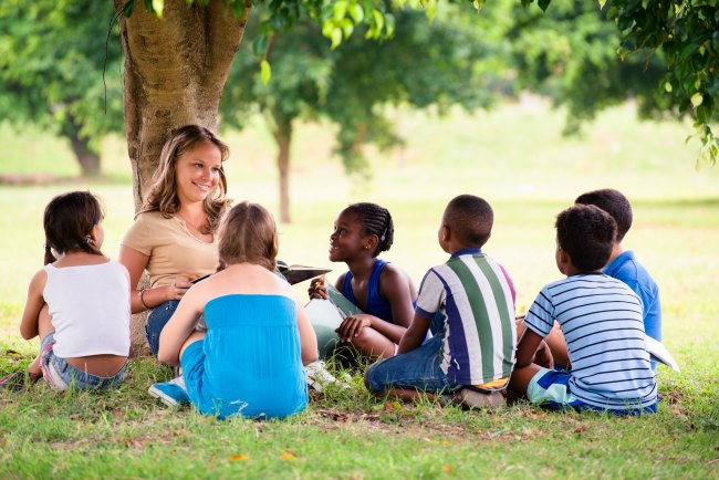 Children sitting under tree listening to adult