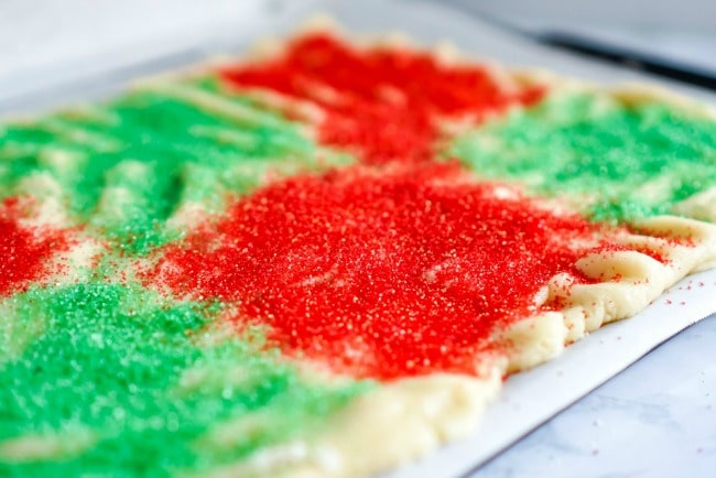 Applying sprinkles on Christmas roll sugar cookies