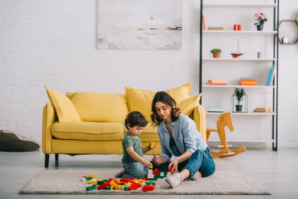 mother playing with son on carpet with legos while working at home