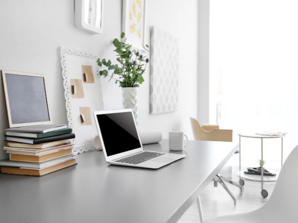 Gray desk with latop and mug and vase with photos on wall in background