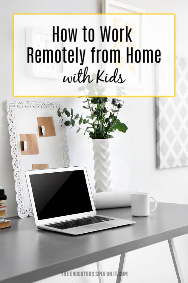 laptop set up on gray desk with plant in vase and photos and clock on wall