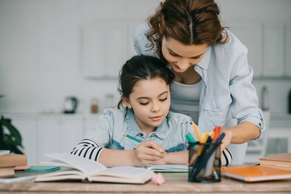 mother helping daughter with school work at table