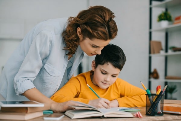 mother helping a child working on school work at home at table
