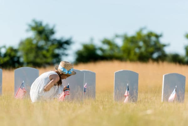 Memorial day with child by visiting soldiers headstones and leaving american flags. 