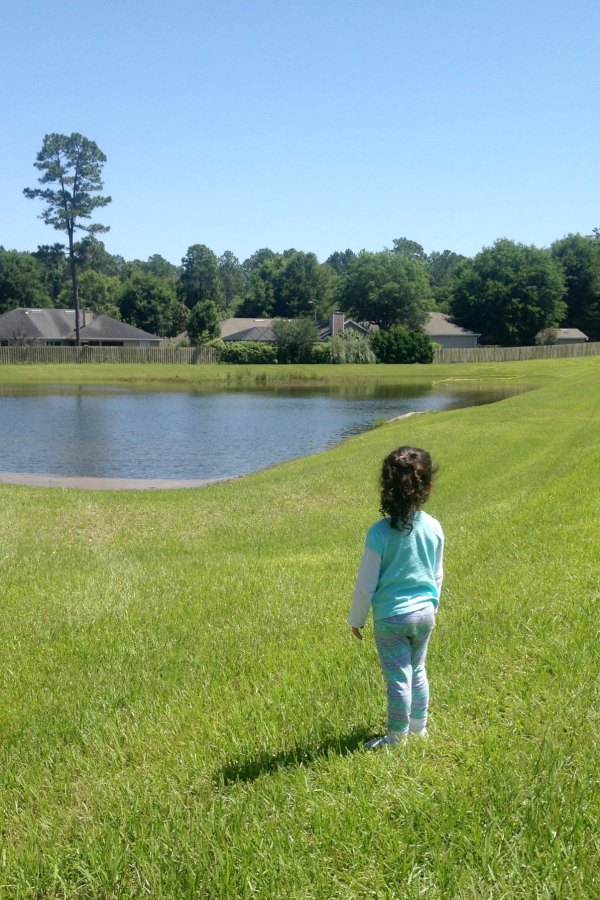 girl standing in grass in backyard looking at retention pond in grassy field