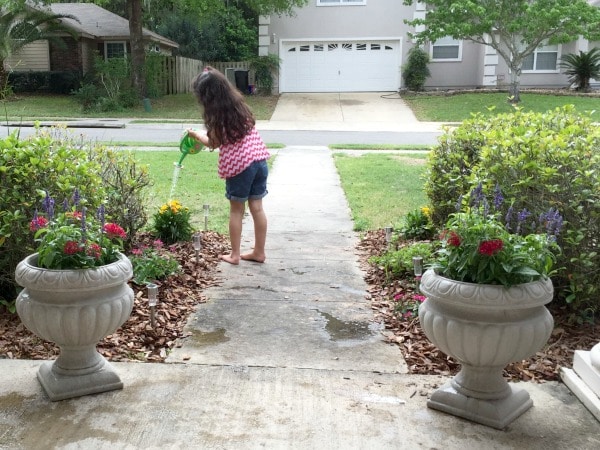 girl watering plants at front yard for butterfly garden