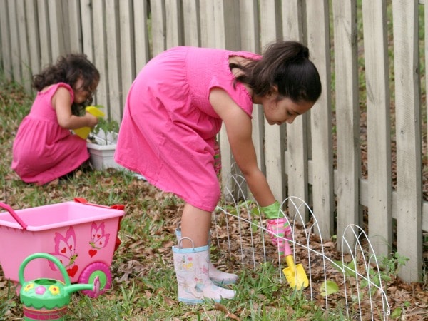 two girls gardening in backyard with gardening tools near fence