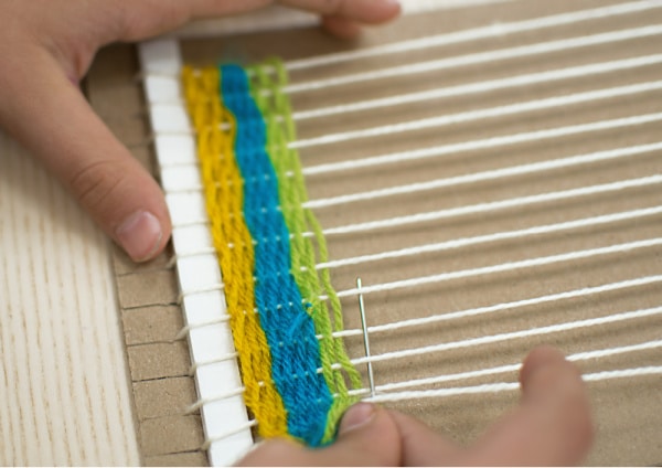 Teaching a child to learn to weave with cardboard loom and colorful yarn. 