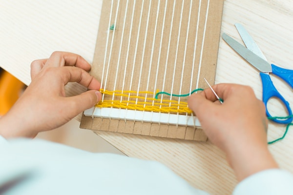 teaching child to weaving with cardboard loom and yarn. 