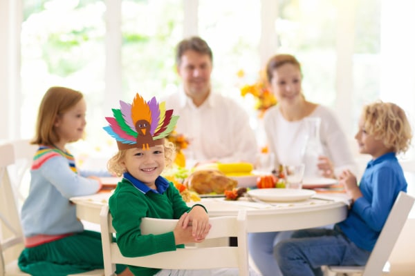 Family with kids eating Thanksgiving dinner. Roasted turkey and pumpkin pie on dining table with autumn decoration. Parents and children festive meal. Father and mother cutting meat. Paper turkey crafts hat.