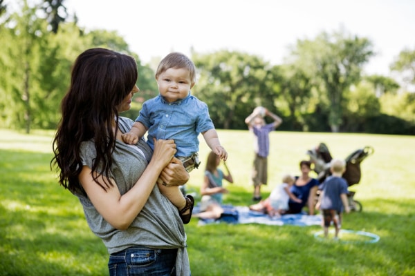 Mom holding child at organized moms group at park with strollers