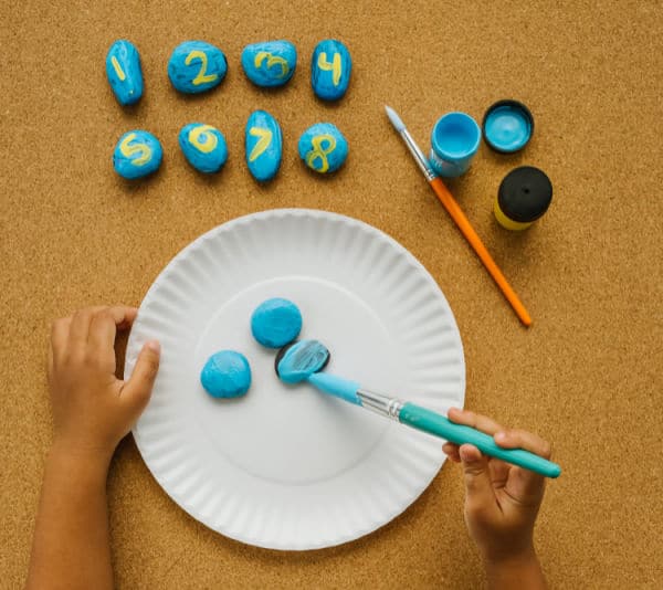 Painting rocks blue and then adding yellow numbers to them for preschool game