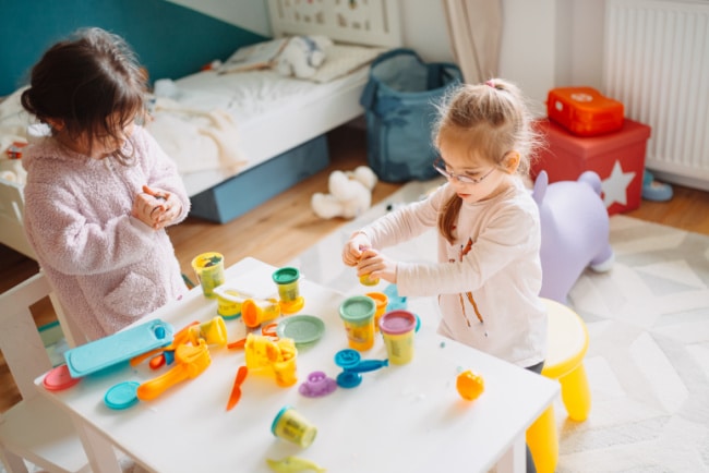 children-playing-with-playdough - The Educators' Spin On It Two young girls play with colorful play-dough and tools at a white table in a bright playroom.